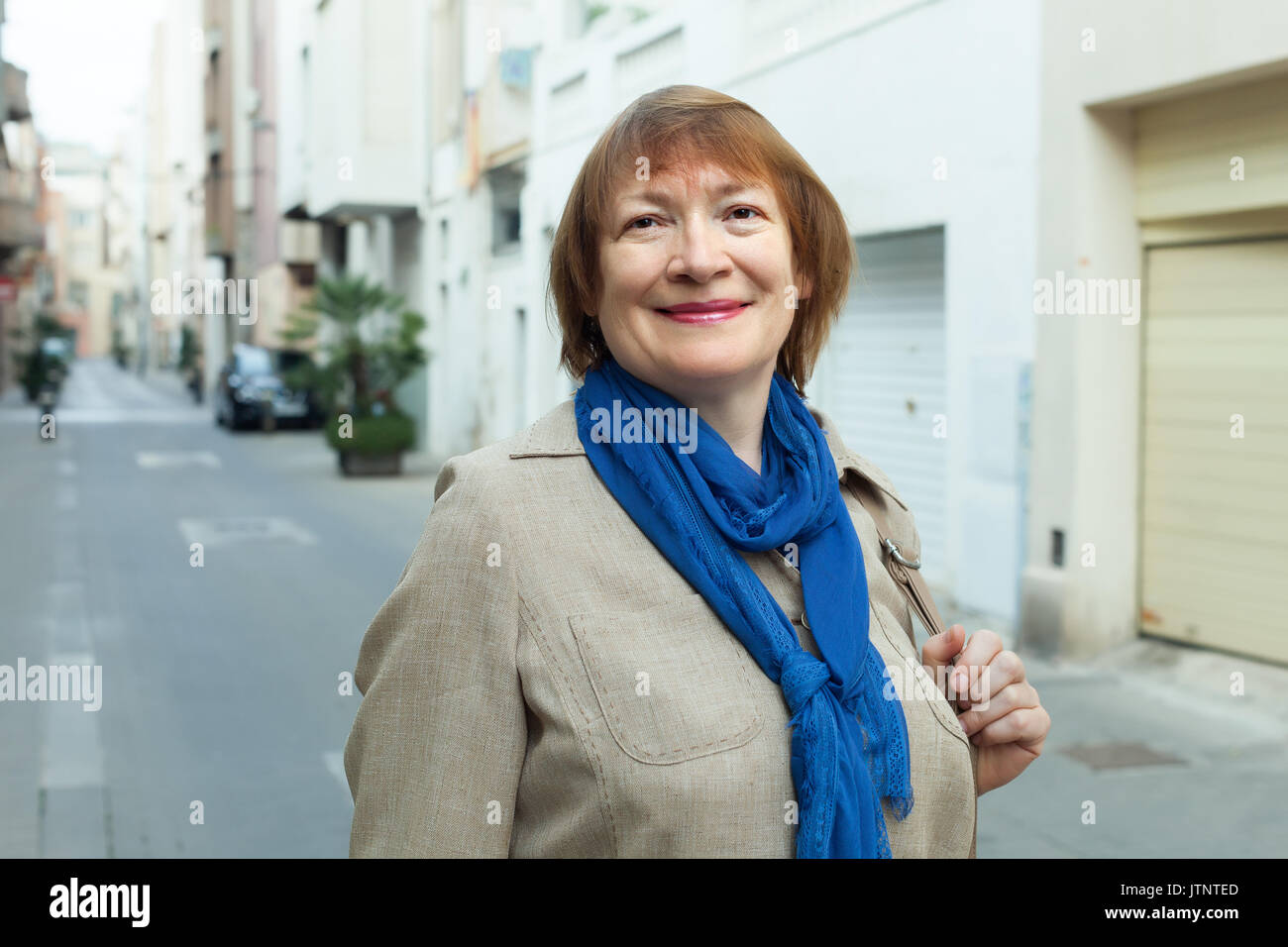positive elderly woman wearing scarf in city street Stock Photo
