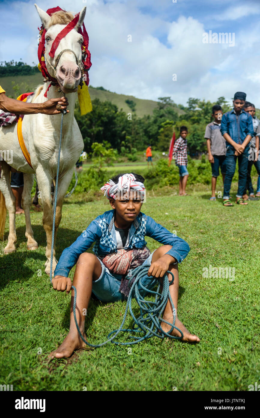 Boy sitting on grass and holding horse at Pasola Festival, Sumba island, Indonesia Stock Photo