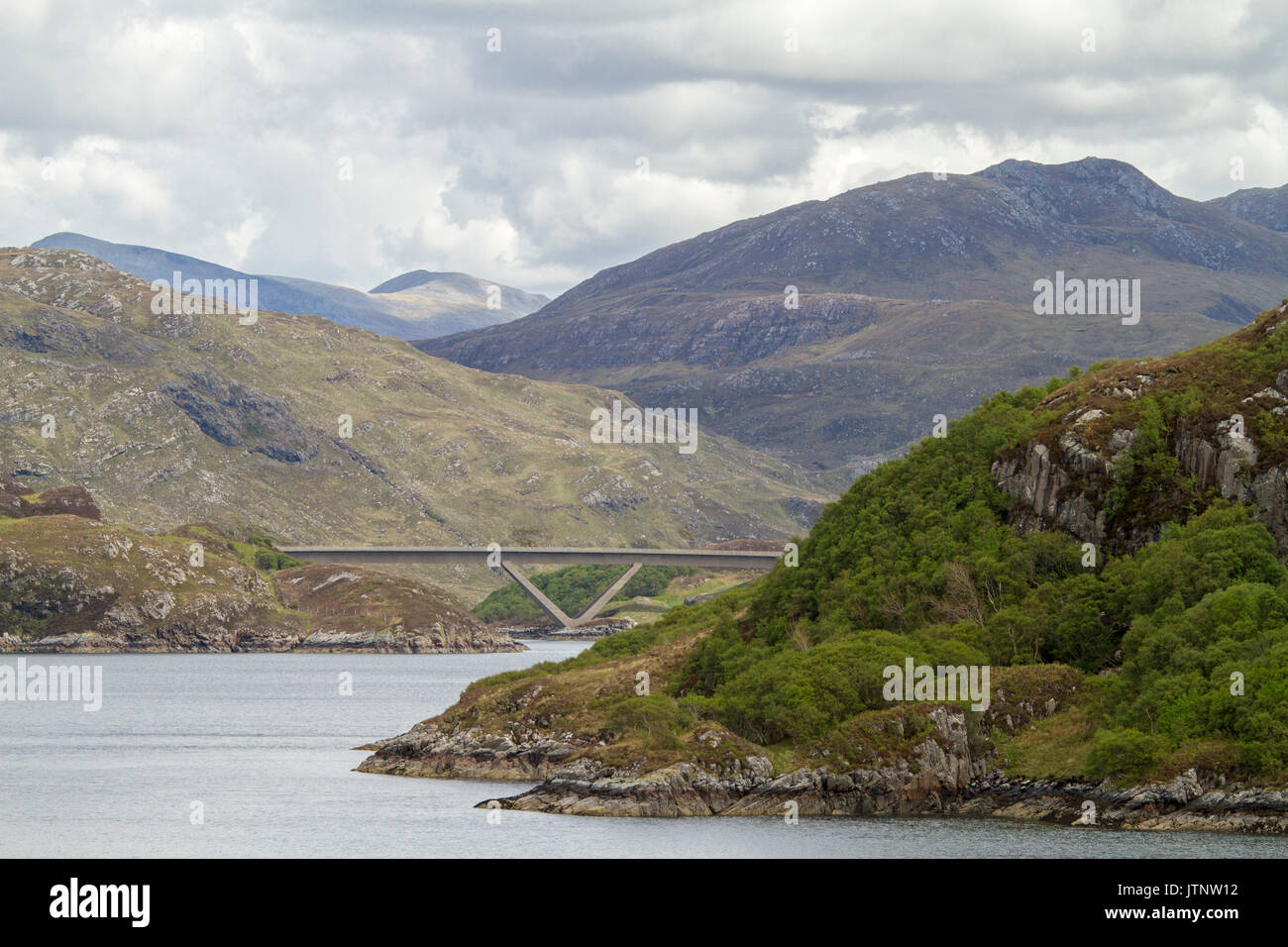 View of unique Kylescu bridge crossing a loch in a landscape dominated by rugged mountains in the highlands of Scotland Stock Photo