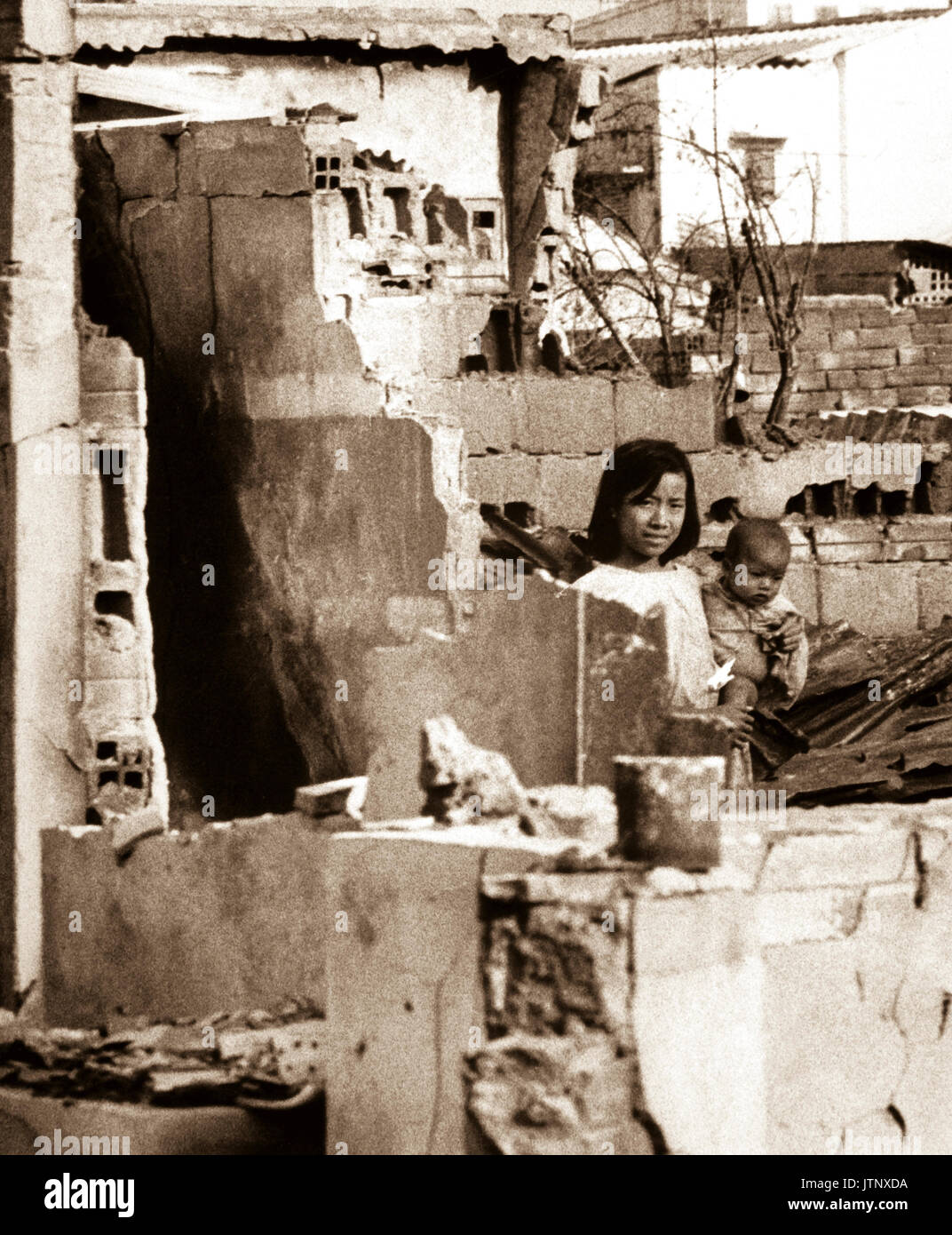 A girl, holding a small child, stands in the ruins of their home after a Viet Cong attack.  Saigon, January 31, 1968.  JUSPAO.  (USIA) NARA FILE #:  306-PSC-68-58 WAR & CONFLICT BOOK #:  422 Stock Photo