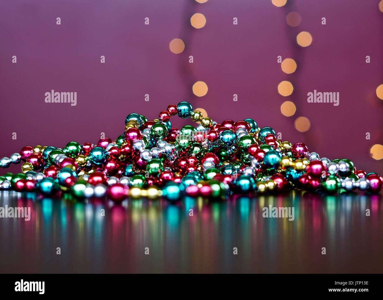 Pile of multi colored Christmas garland with reflections and blurred lights in background Stock Photo