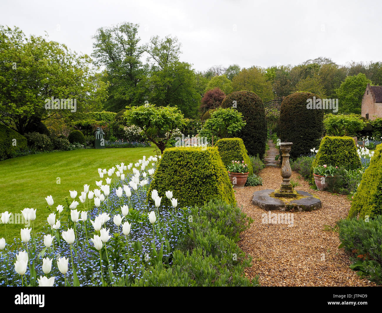 Sundial path through Chenies Manor Garden at tulip time with lawn and pavilion building.Hedges, topiary and shingle path through the beautiful garden. Stock Photo