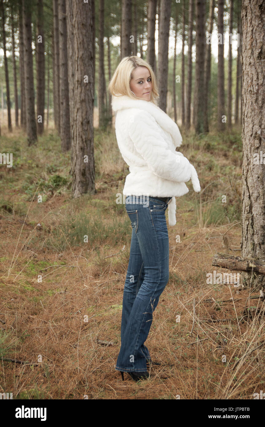 Pretty blonde girl in a forest wearing jeans and a white jacket Stock Photo  - Alamy