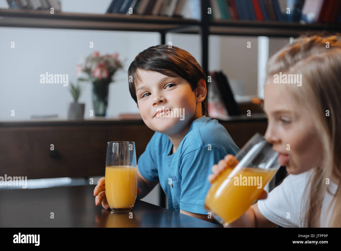 little boy and girl drinking orange juice at kitchen together Stock Photo