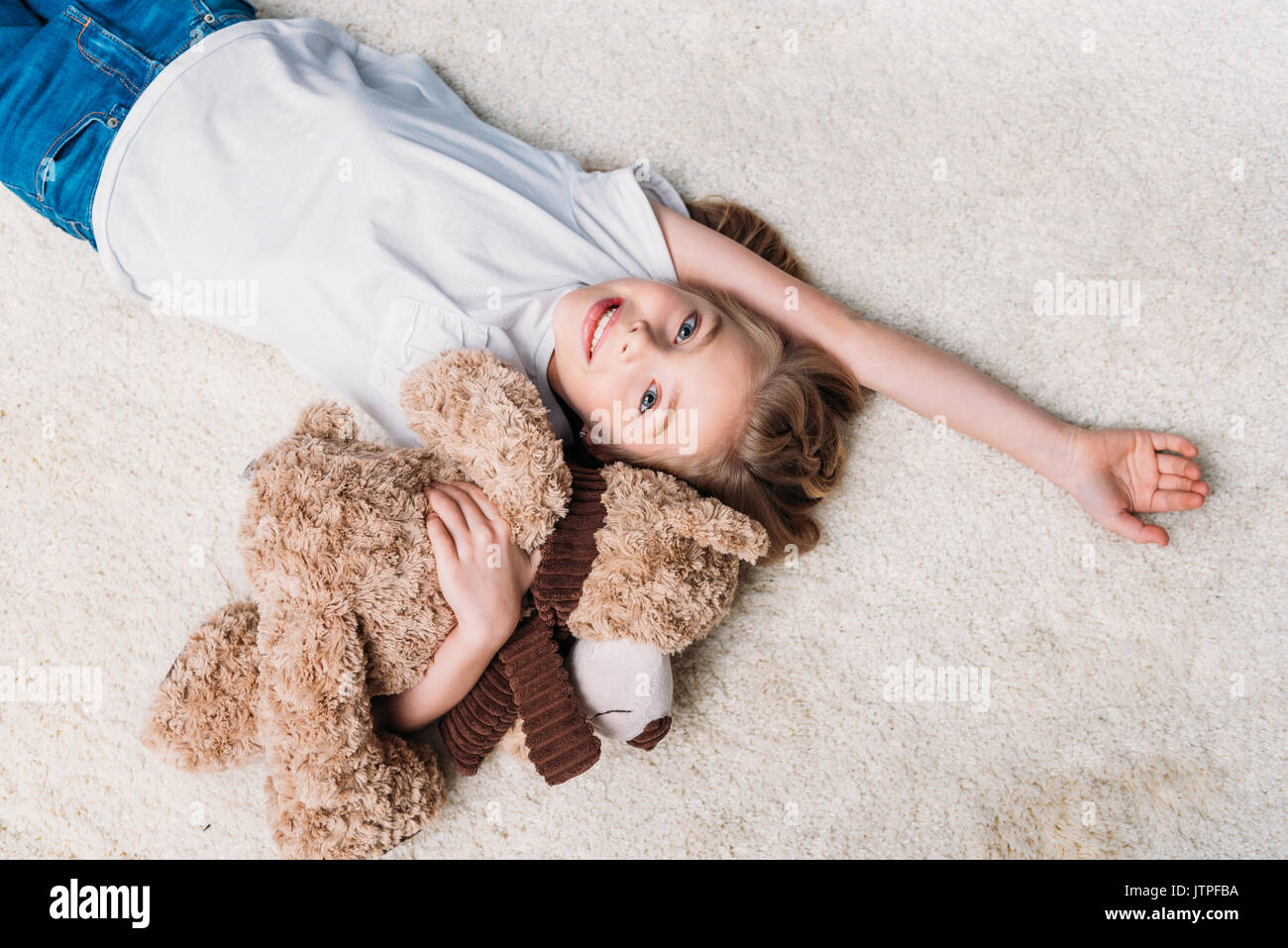 little girl holding teddy bear and looking at camera while lying on ...