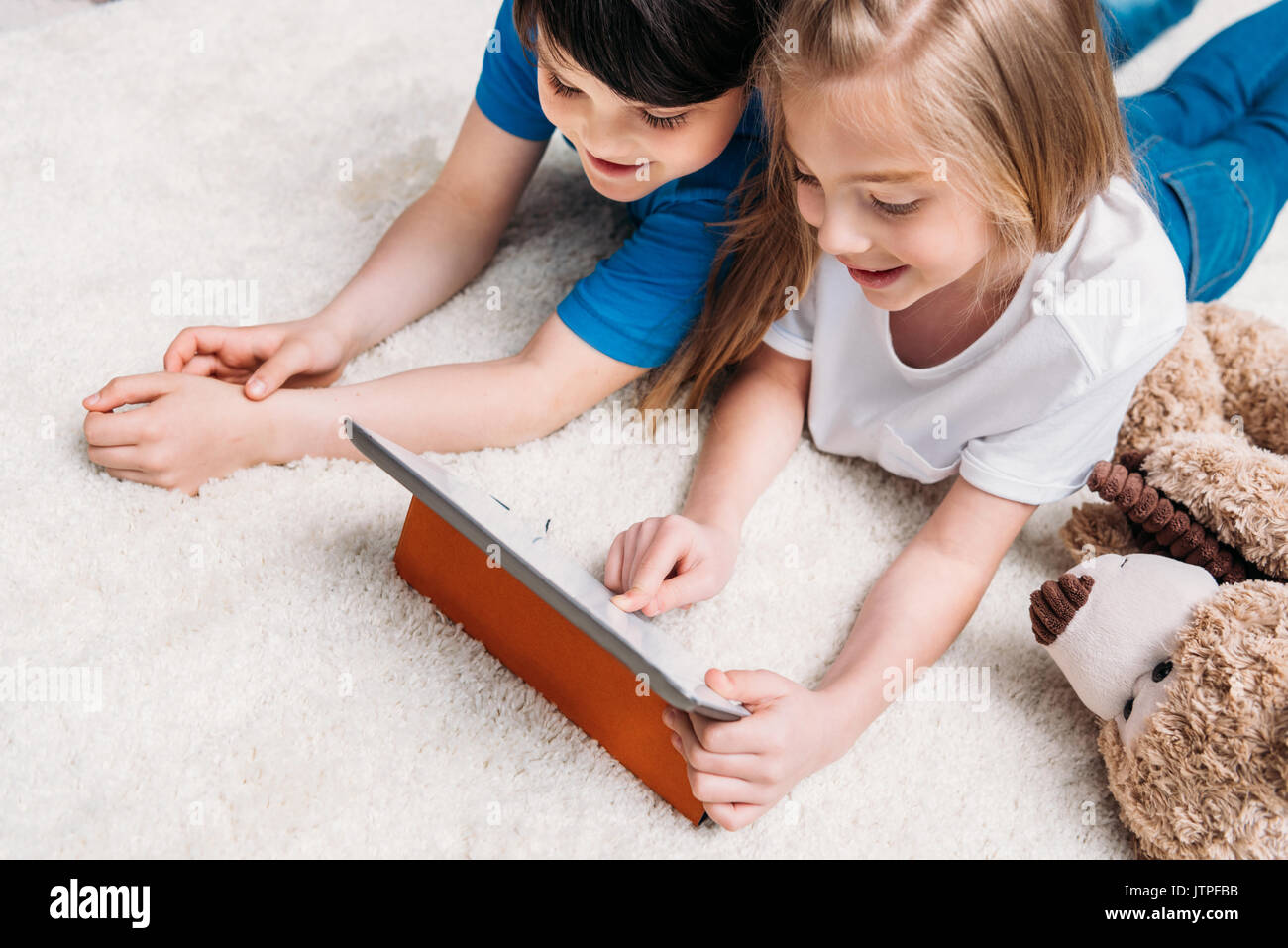 little boy and girl playing with digital tablet while lying on carpet ...