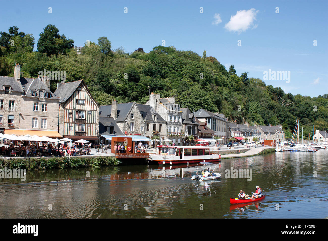 France. Brittany. Dinan. Harbourside houses and restaurants by River Rance with tourists in canoe and motor boat. Stock Photo