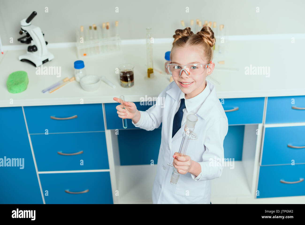 schoolgirl in goggles holding reagents in flasks in chemical lab
