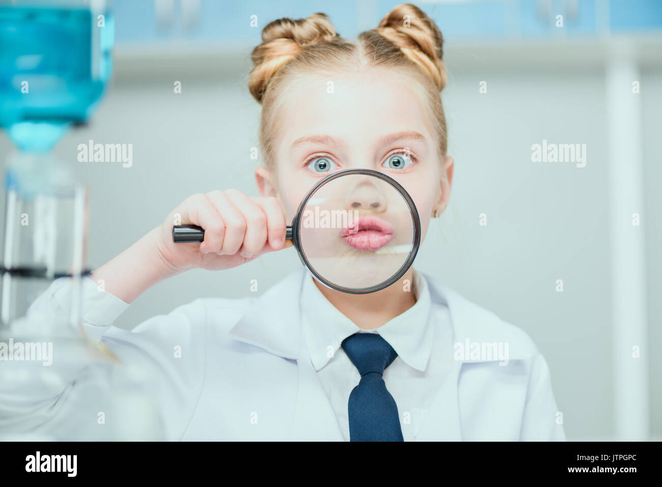 Little scientist in white coat holding magnifier in chemical lab, science school concept Stock
