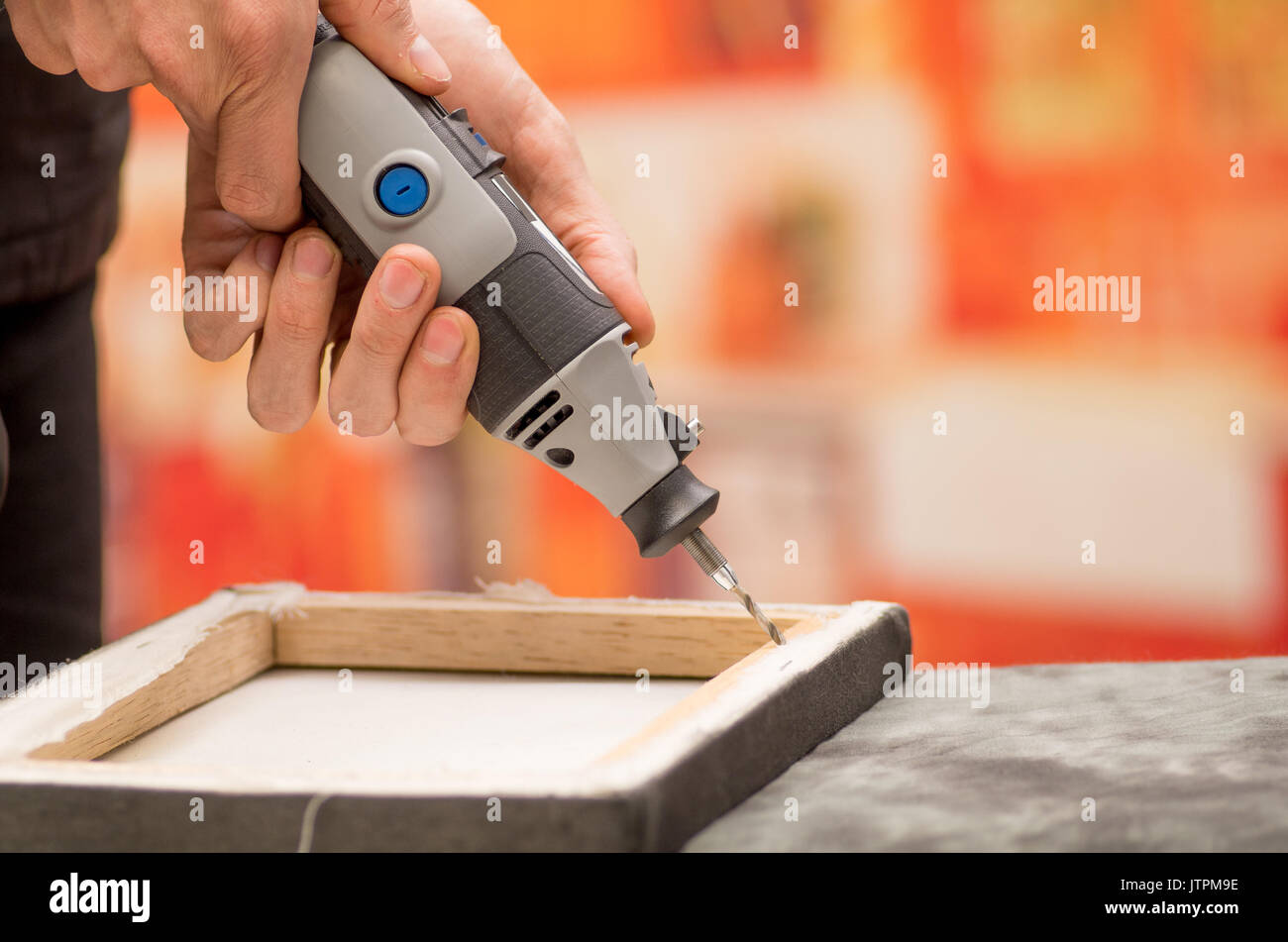 Closeup of a hardworker man drilling a wooden frame with his drill over a gray table in a blurred background Stock Photo
