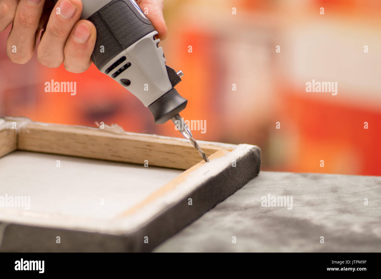 Closeup of a hardworker man drilling a wooden frame with his drill over a gray table in a blurred background Stock Photo