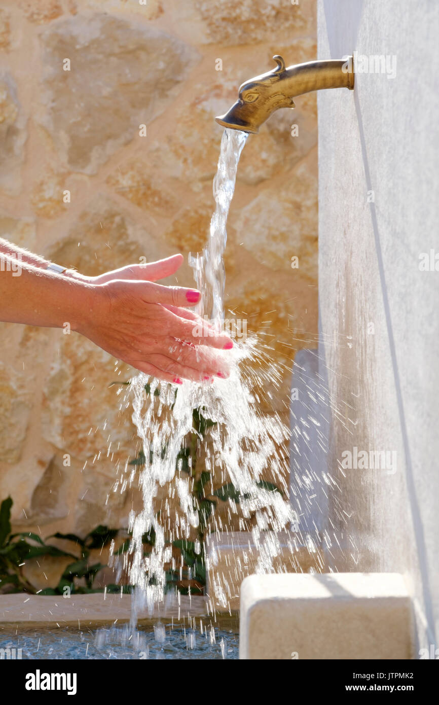 A woma washing her hands under cold running water from an ornamental outdoor tap Stock Photo