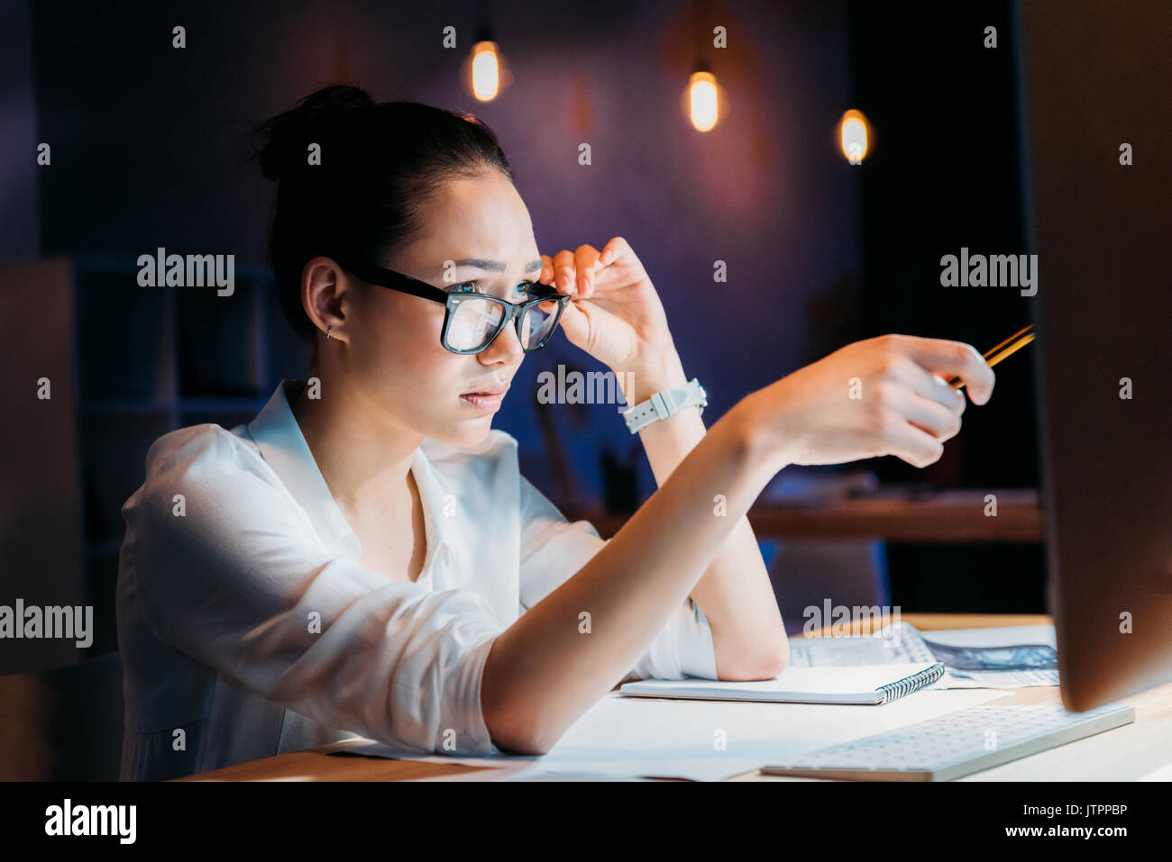 concentrated asian businesswoman in eyeglasses pointing at computer