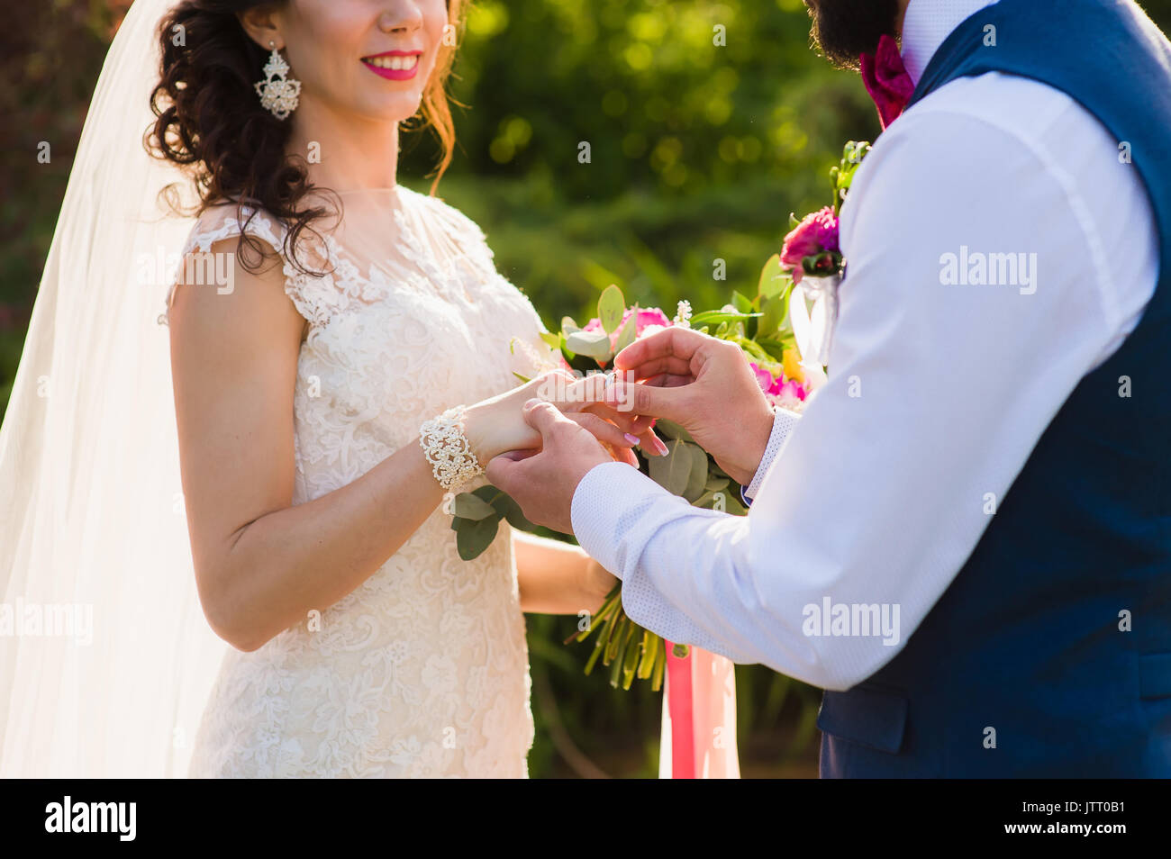 Groom wears ring on bride's finger. Newlyweds exchange rings on registration of marriage in the open air. Close-up of man putting a ring on womans fin Stock Photo