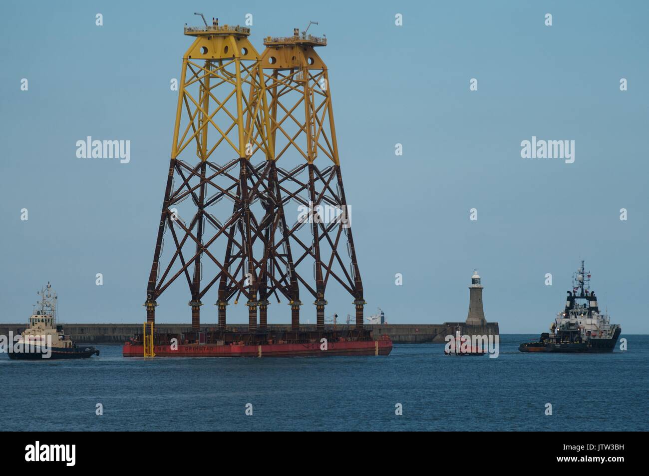 River Tyne, South Shields, UK, 10th August 2017. Wind turbine foundations pass Tynemouth pier and lighthouse on their way to the Beatrice offshore wind farm in the Moray Firth. Due to their height National Grid had to raise the height of power cables across the Tyne despite the pylons being two of the highest in Britain, surpassed only by sets spanning the River Thames near London and the River Severn in Bristol. Credit: Colin Edwards/Alamy Live News. Stock Photo