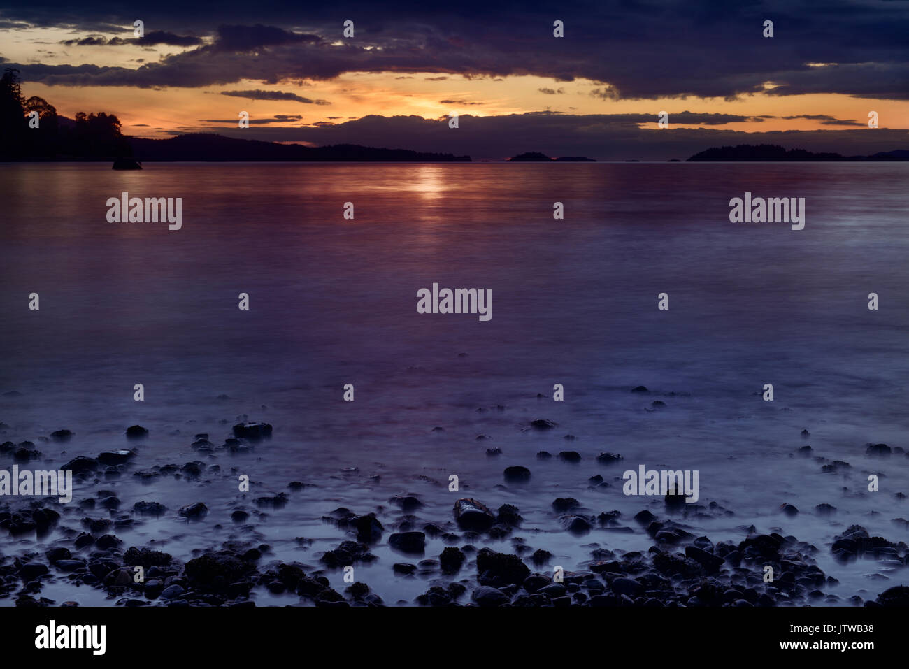 Dramatic sunset sky and ocean shore pebbles over the Strait of Georgia, Salish Sea, Pacific Ocean in Nanaimo, Vancouver Island, BC, Canada Stock Photo