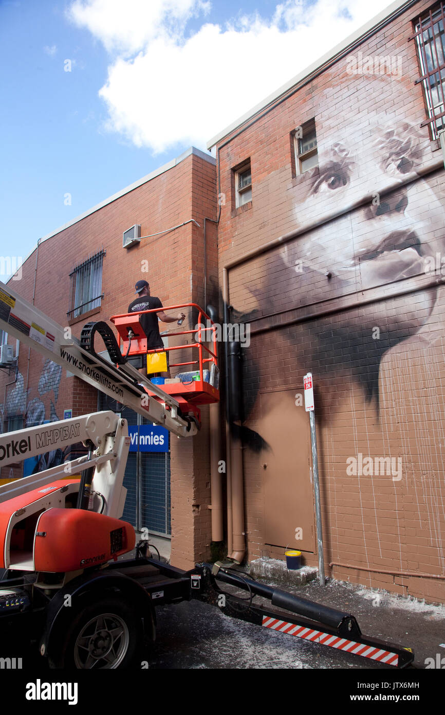 Street artist spraypainting a mural in Lismore's Back Alley Gallery