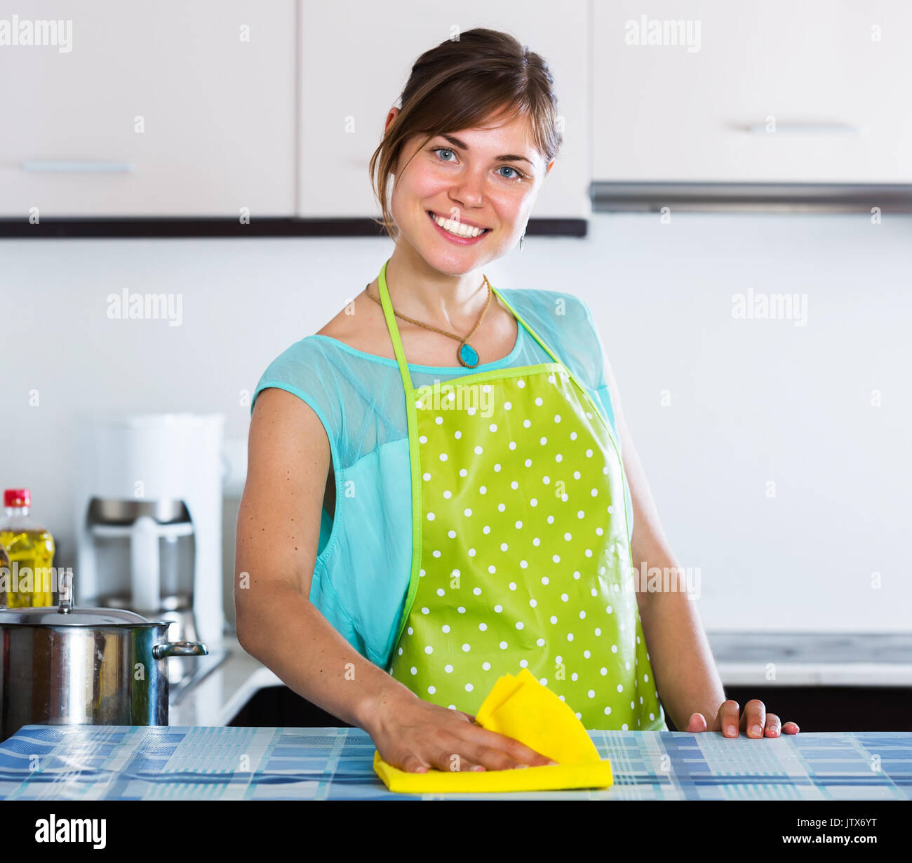 Happy adult girl dusting surfaces in residential kitchen Stock Photo