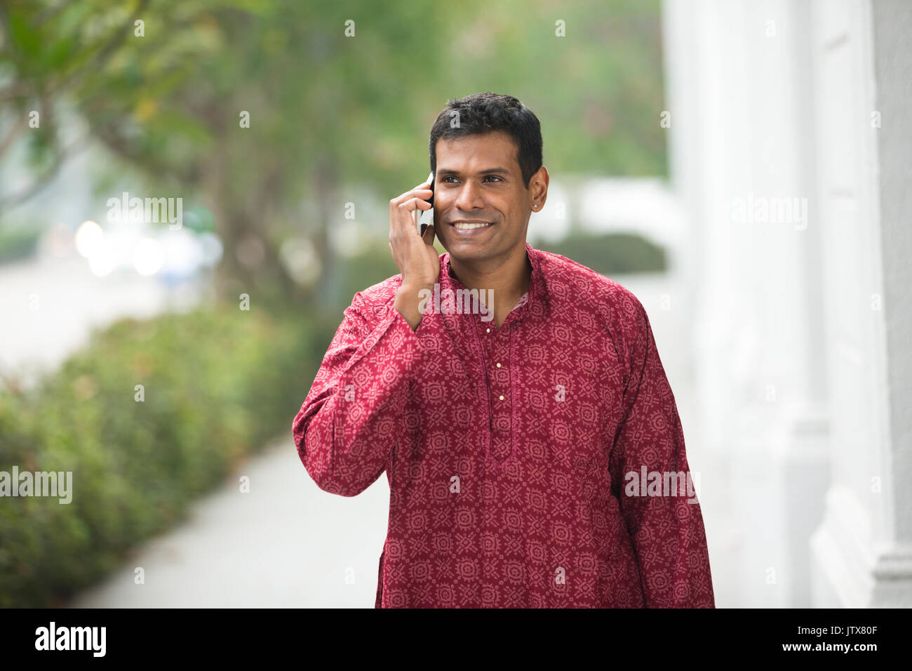 Happy Indian man using a smart phone on street. Traditional indian male wearing a kurta with smart phone outside. Stock Photo