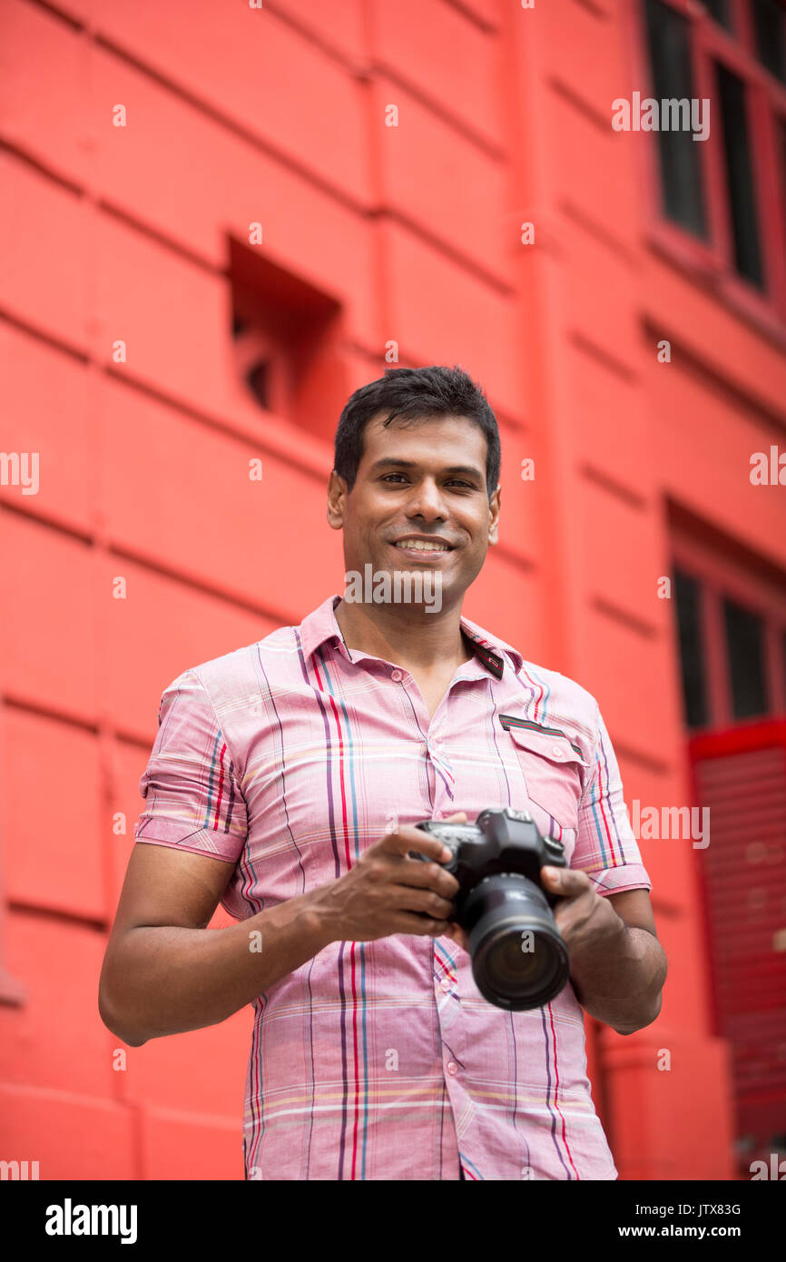 Portrait of happy Indian man taking photos with a camera in the city. Asian Photographer shooting outside with digital camera. Stock Photo