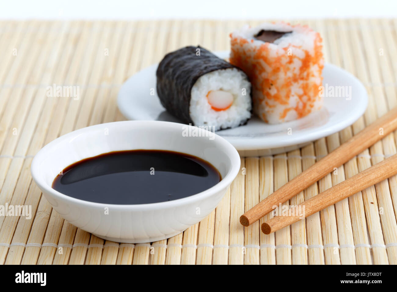 Soya sauce in white bowl on bamboo mat with chopsticks and sushi on
