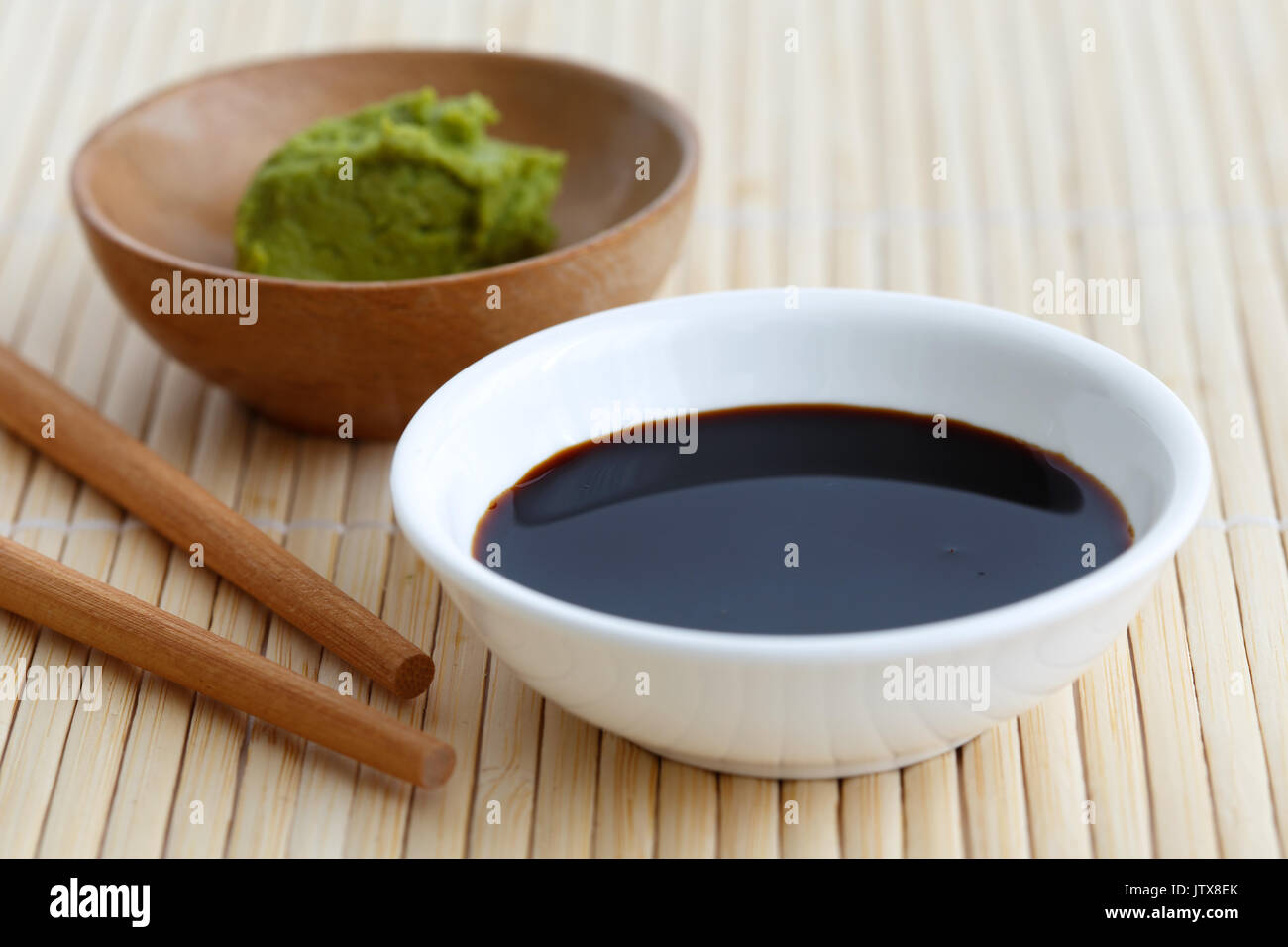 Soya sauce in white bowl on bamboo mat with chopsticks and wasabi Stock