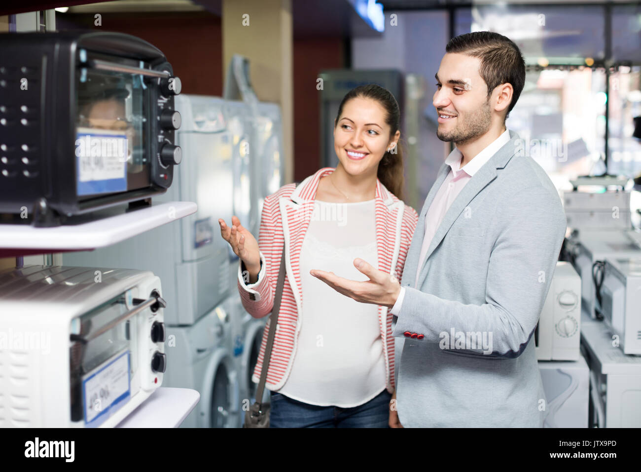 Happy smiling couple choosing new microwave oven in hypermarket . Focus on guy Stock Photo