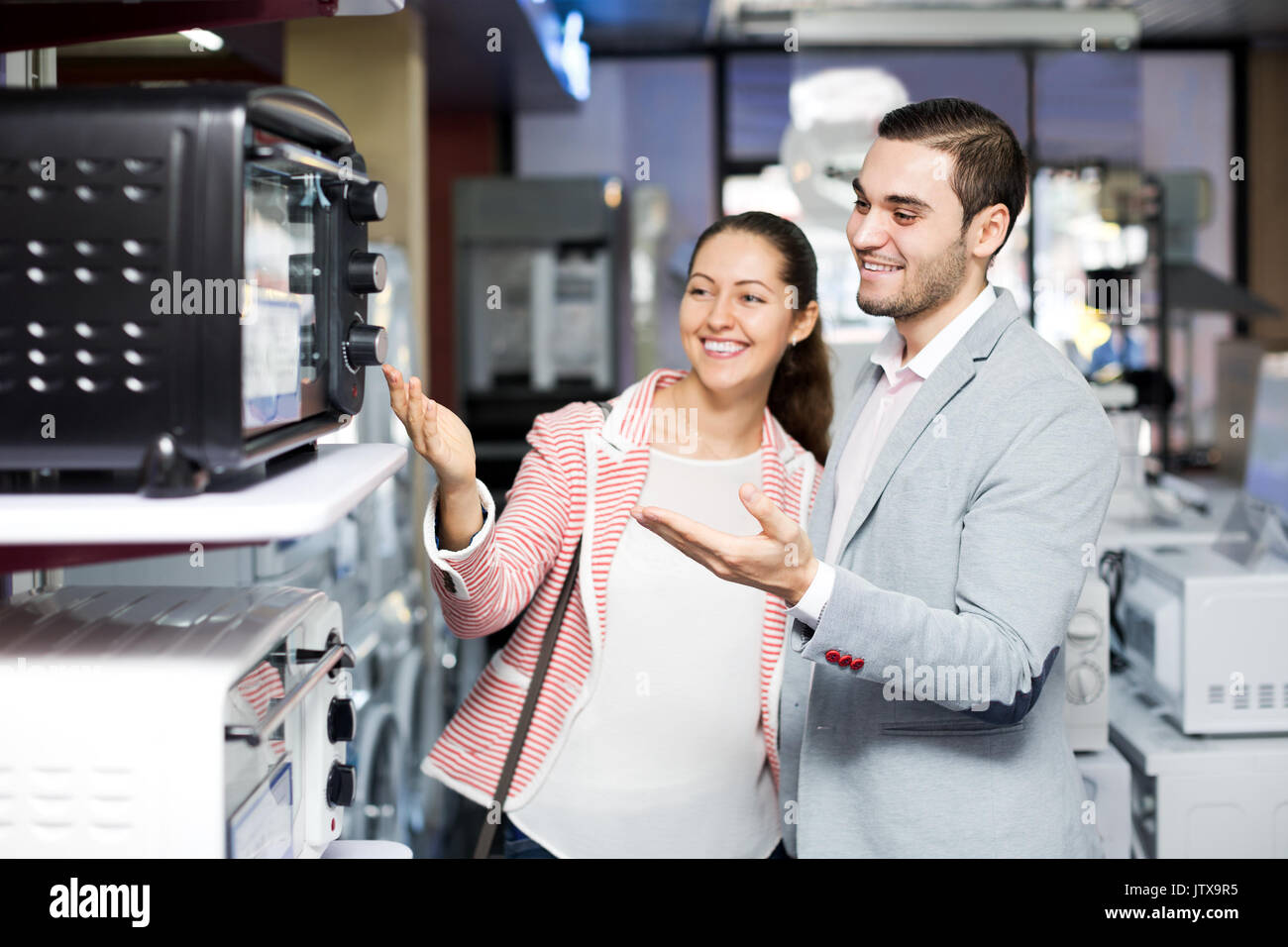 Cheerful family couple choosing new microwave in supermarket. Focus on the man Stock Photo