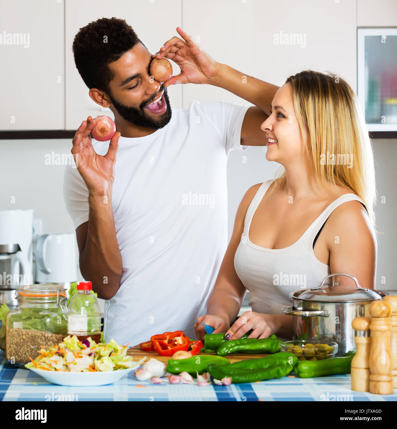 Young interracial couple cooking vegetables and laughing in home interior. Focus on man Stock Photo