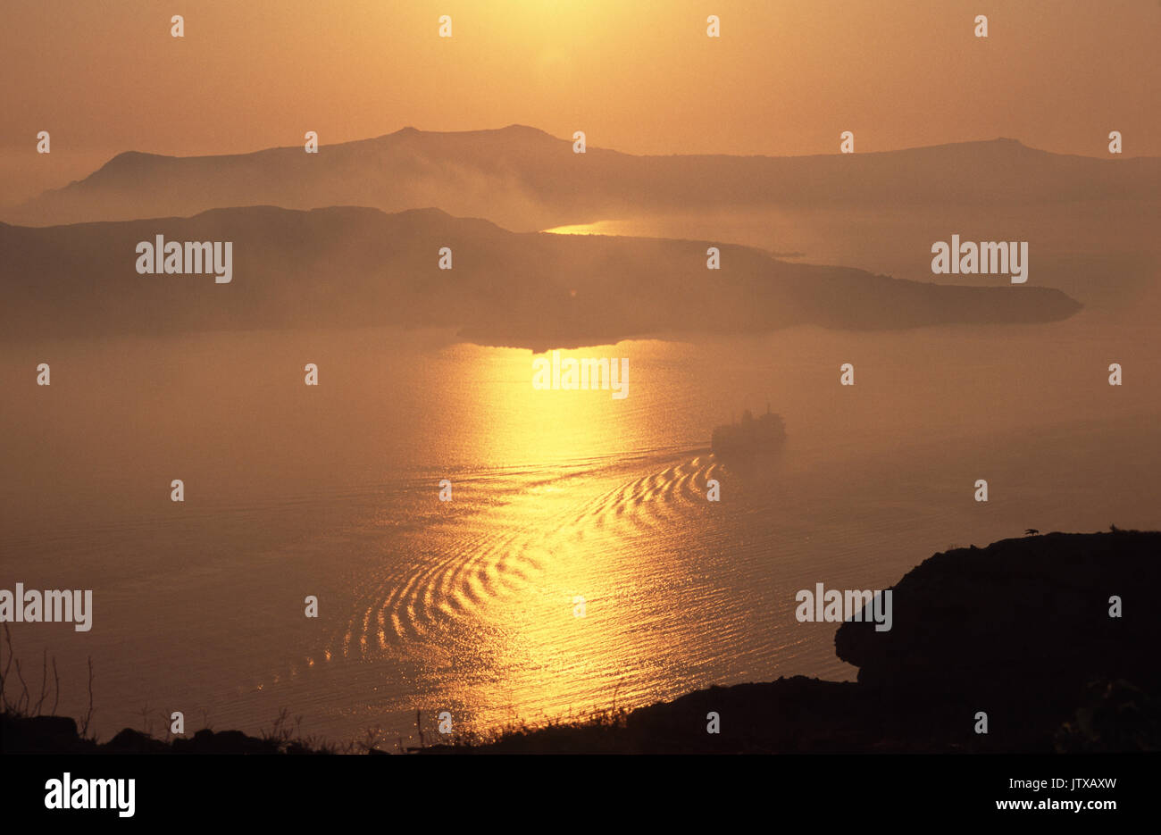 Santorin: Fährschiff im aufsteigenden Dunst in der Abendsonne, vor den Inseln der Caldera, Nea Kameni, Palea Kameni ; vessel passing below  at sunset Stock Photo