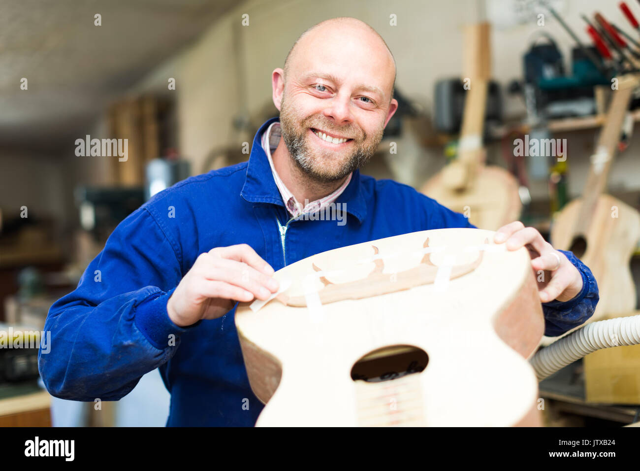 Successful guitar maker in a process of making an a acoustic guitar in a workshop. He is looking to the camera and cheking guitar's case Stock Photo