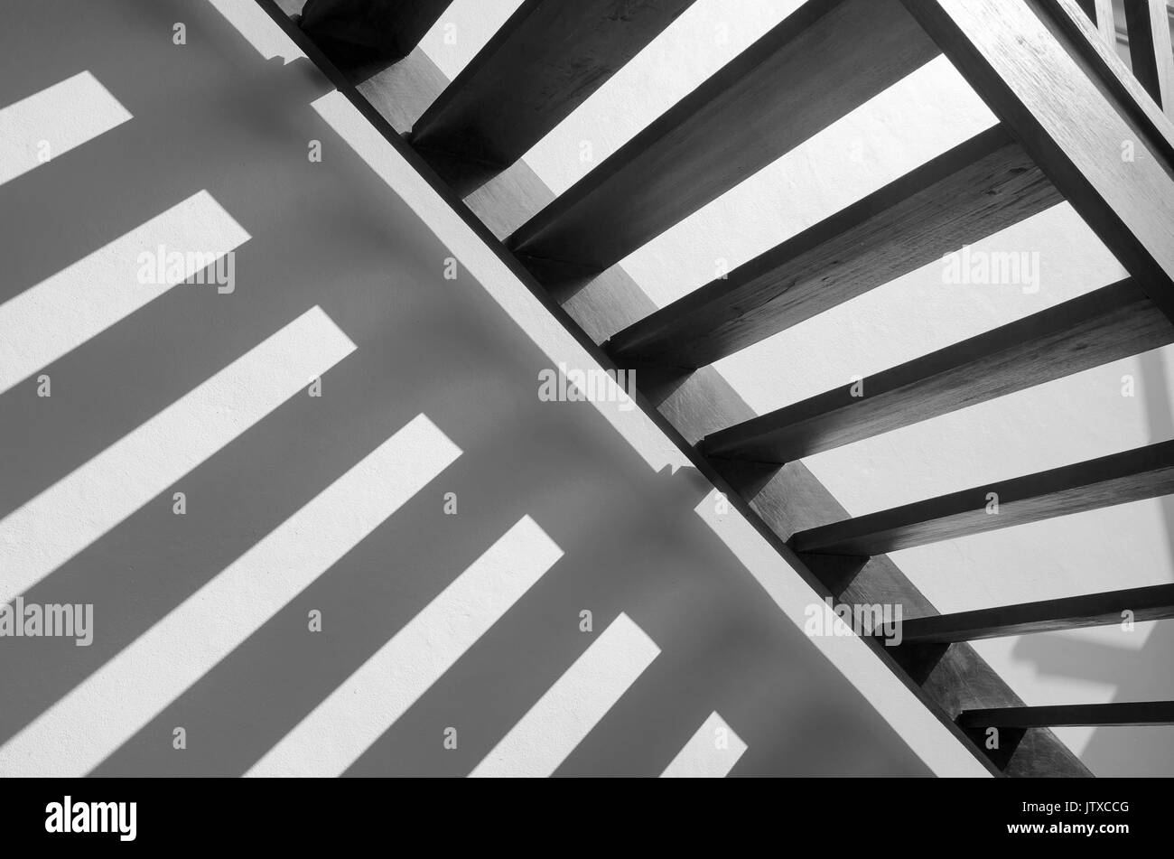 Shadow stripes light on white concrete wall of Thai traditional style wooden stair in the morning light. Black and white Multiple exposure lighting Stock Photo
