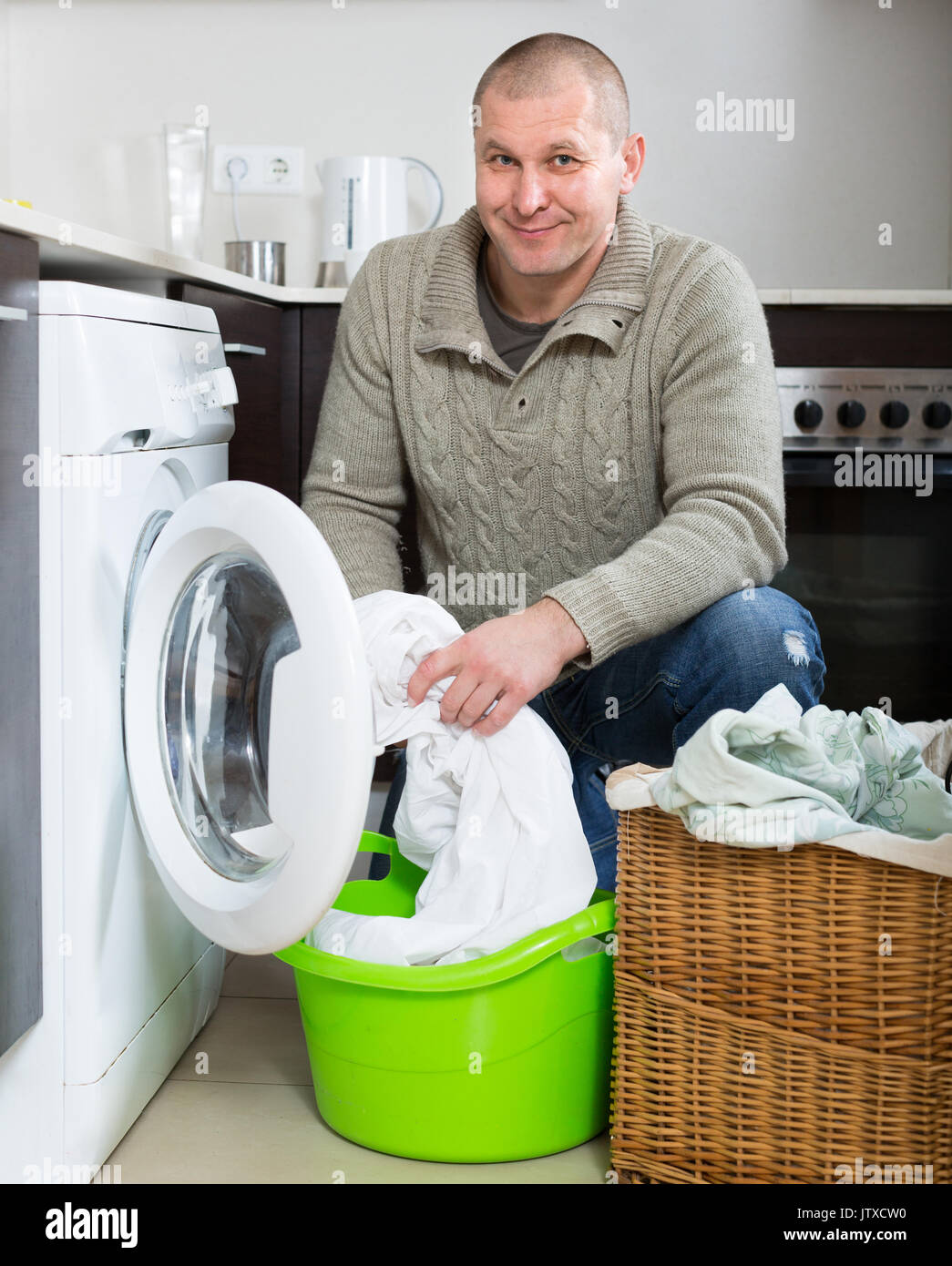 Home laundry. Ordinary smiling man using washing machine at home Stock Photo