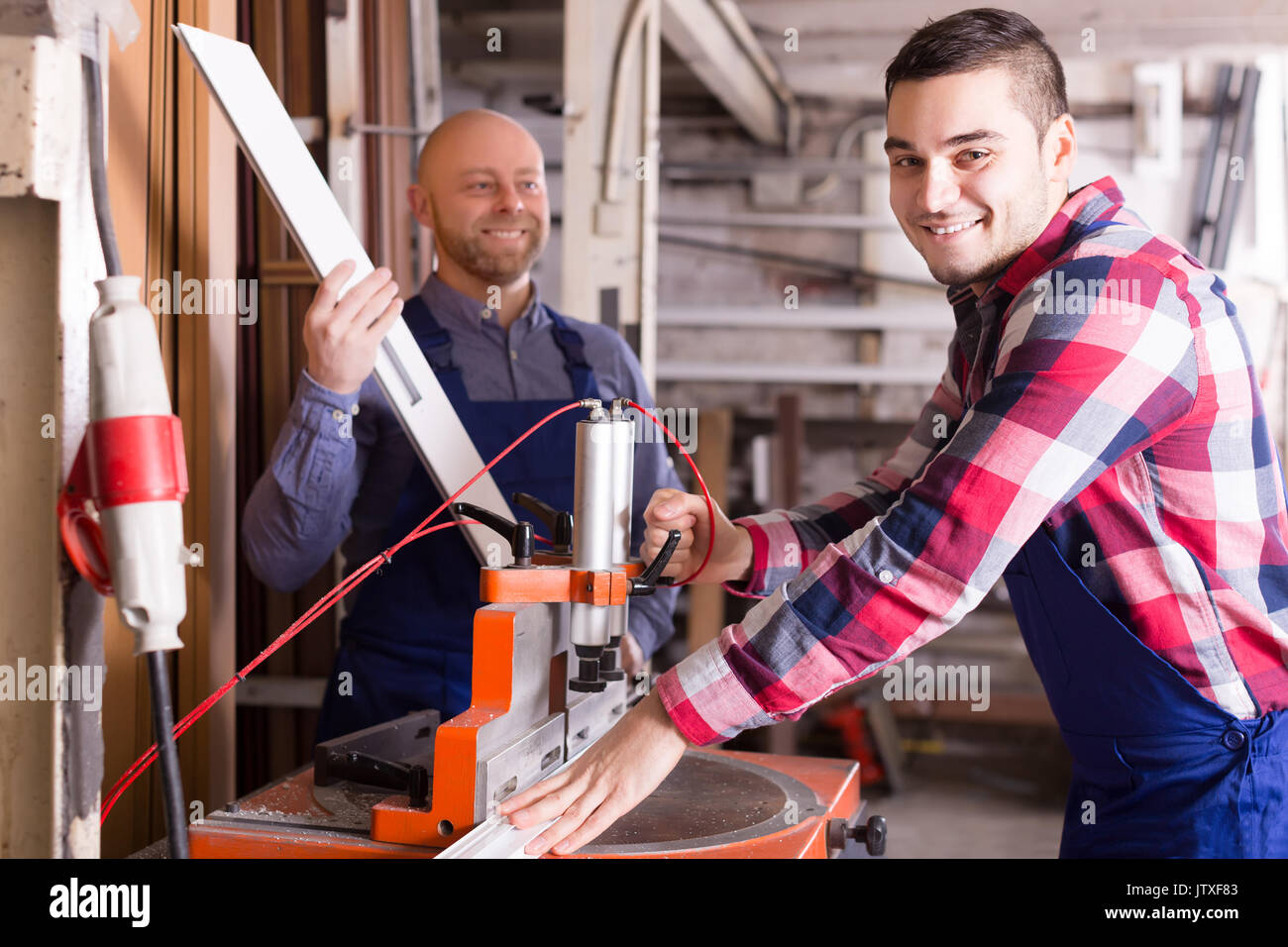 Two positive workmen working on a machine in PVC shop Stock Photo