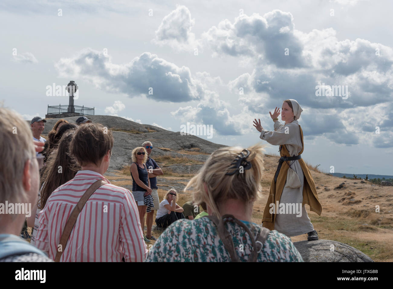 A guide, in historical clothing, is talking about the vikings and their life at the Birka outdoor museum. The Ansgar monument is in the background. Stock Photo
