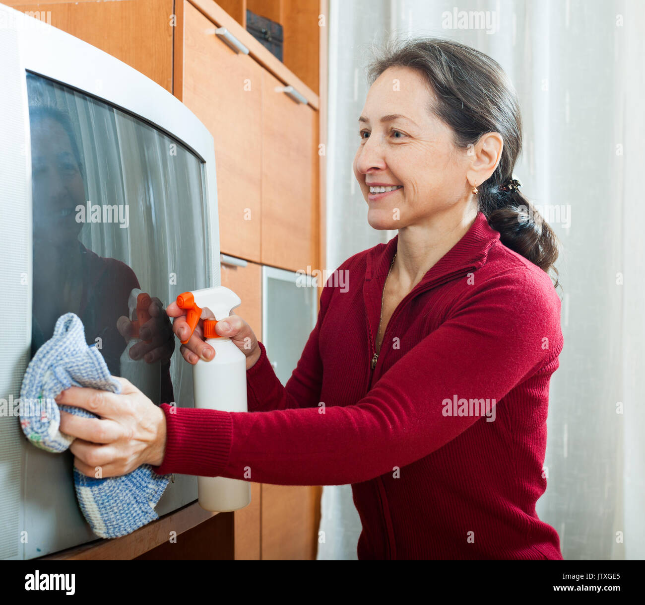Smiling mature woman cleaning TV at home Stock Photo Alamy