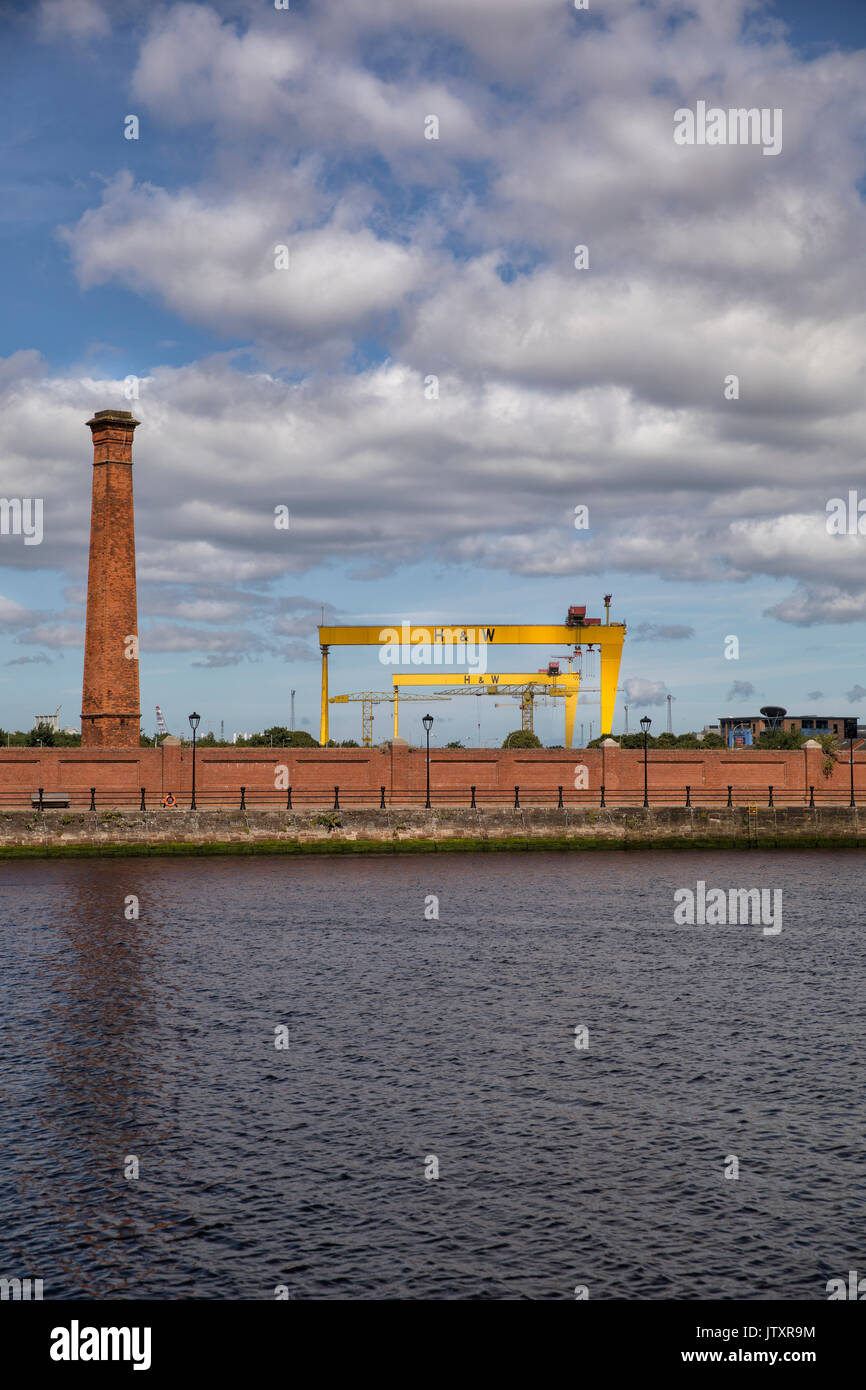 Belfast, a view of the old shipyard, Harland and Wolff Cranes (Samson and Goliath) with river Lagan, chimney stack and red brick wall in foreground Stock Photo
