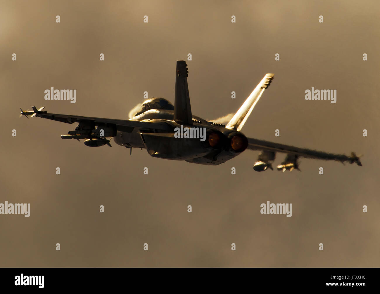 Rear end sunset shot of an F/A18 Super Hornet with afterburners at takeoff. Condensation vortices are visible near the wing roots. Stock Photo