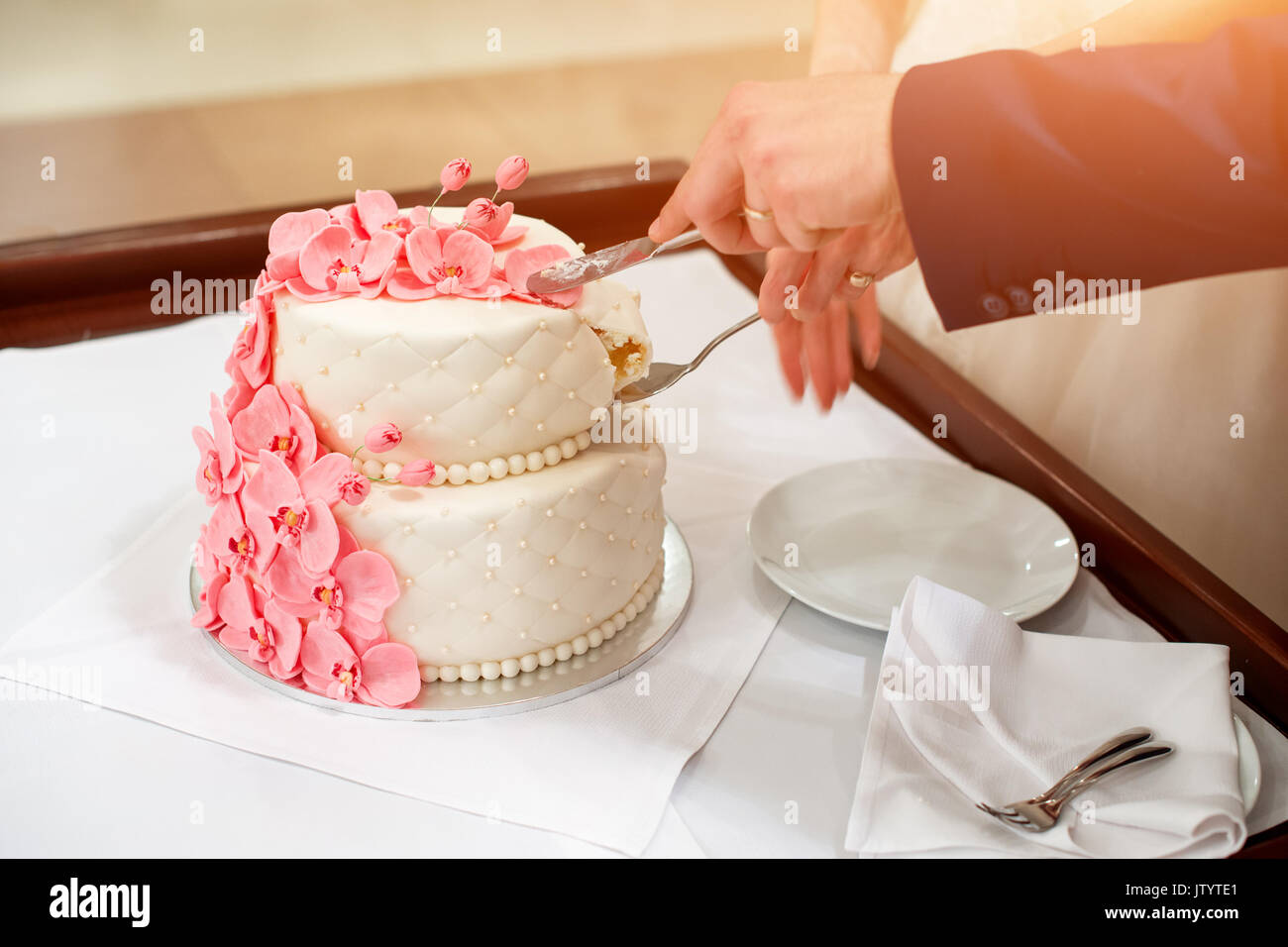 Bride and groom cutting their wedding cake decorated with orchids. Stock Photo