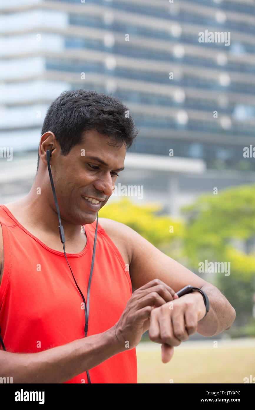 Sporty Indian man looking at his smartwatch heart rate monitor. Athletic Asian man using a smart watch and listening to music with earphones Stock Photo Alamy