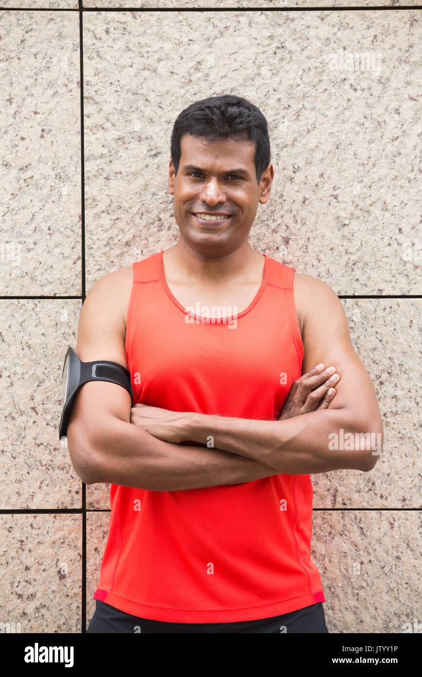 Portrait of athletic Indian man resting after urban run through city streets. Asian male runner taking break standing relaxing. Stock Photo
