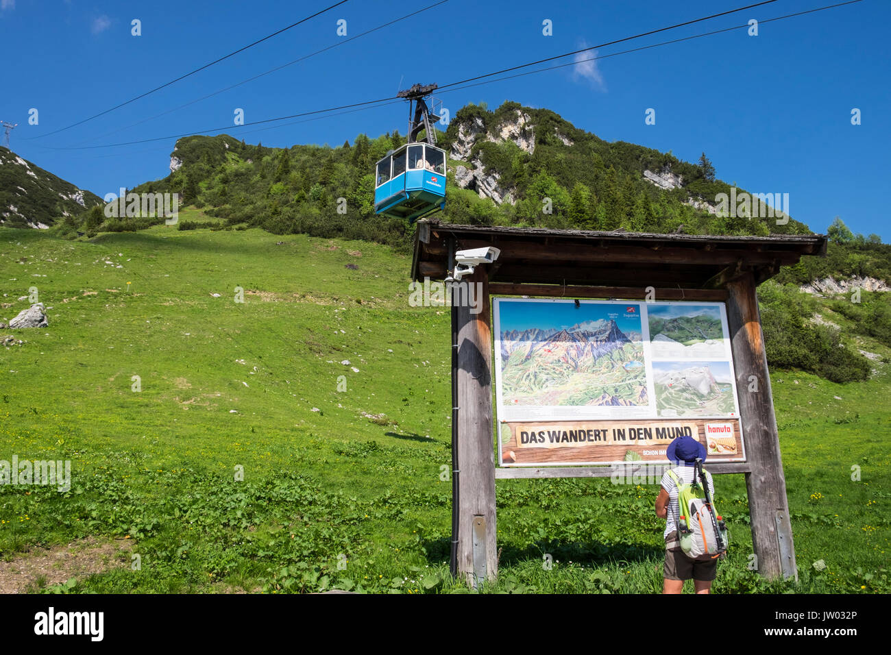 Woman walker reading information panel as Hochalmbahn cable car cabin is coming down the mountain, Hochalm, Kreuzeck, Zugspitzland, Bavaria, Germany Stock Photo