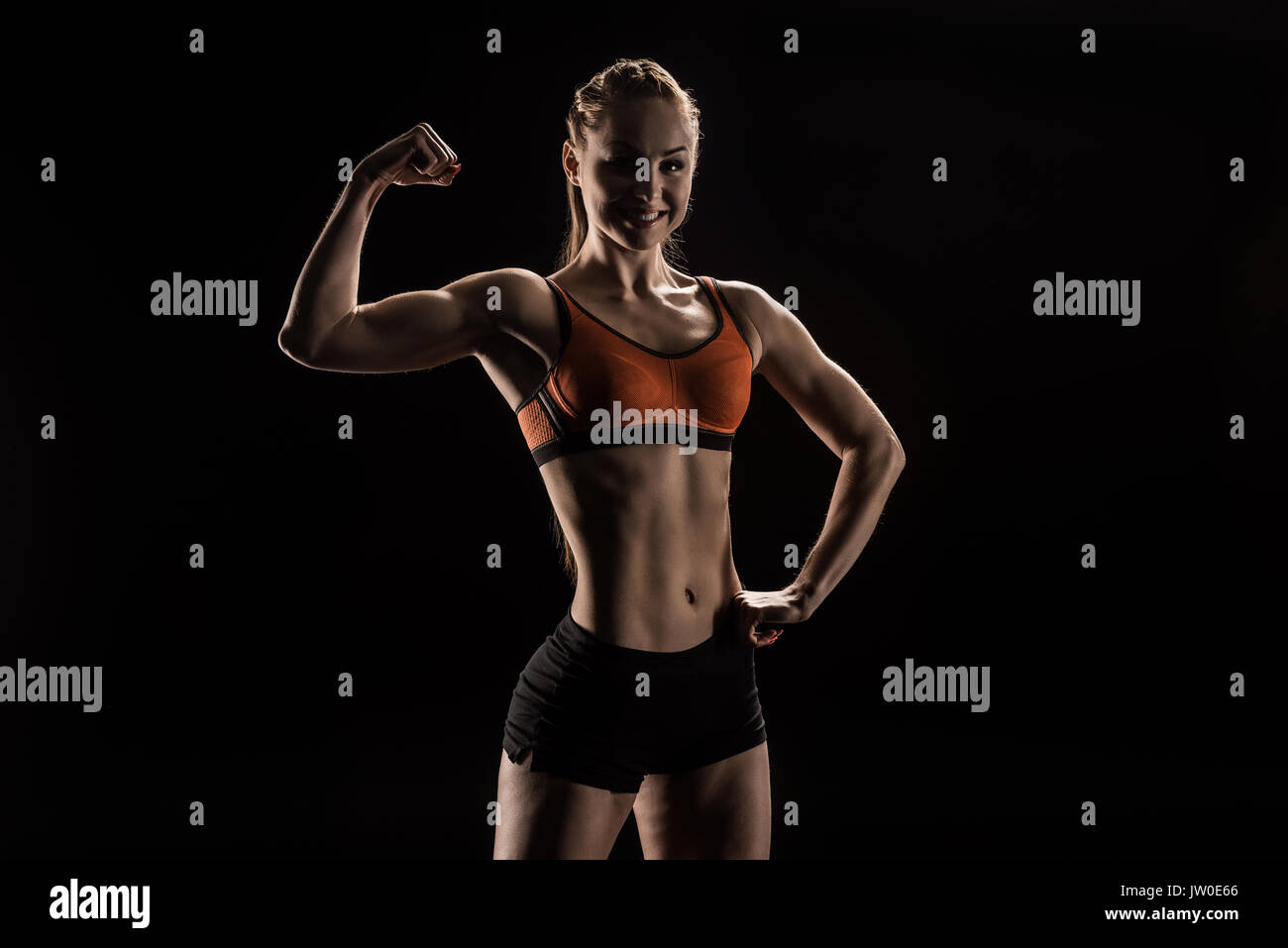 young smiling sportswoman flexing biceps and looking at camera Stock Photo