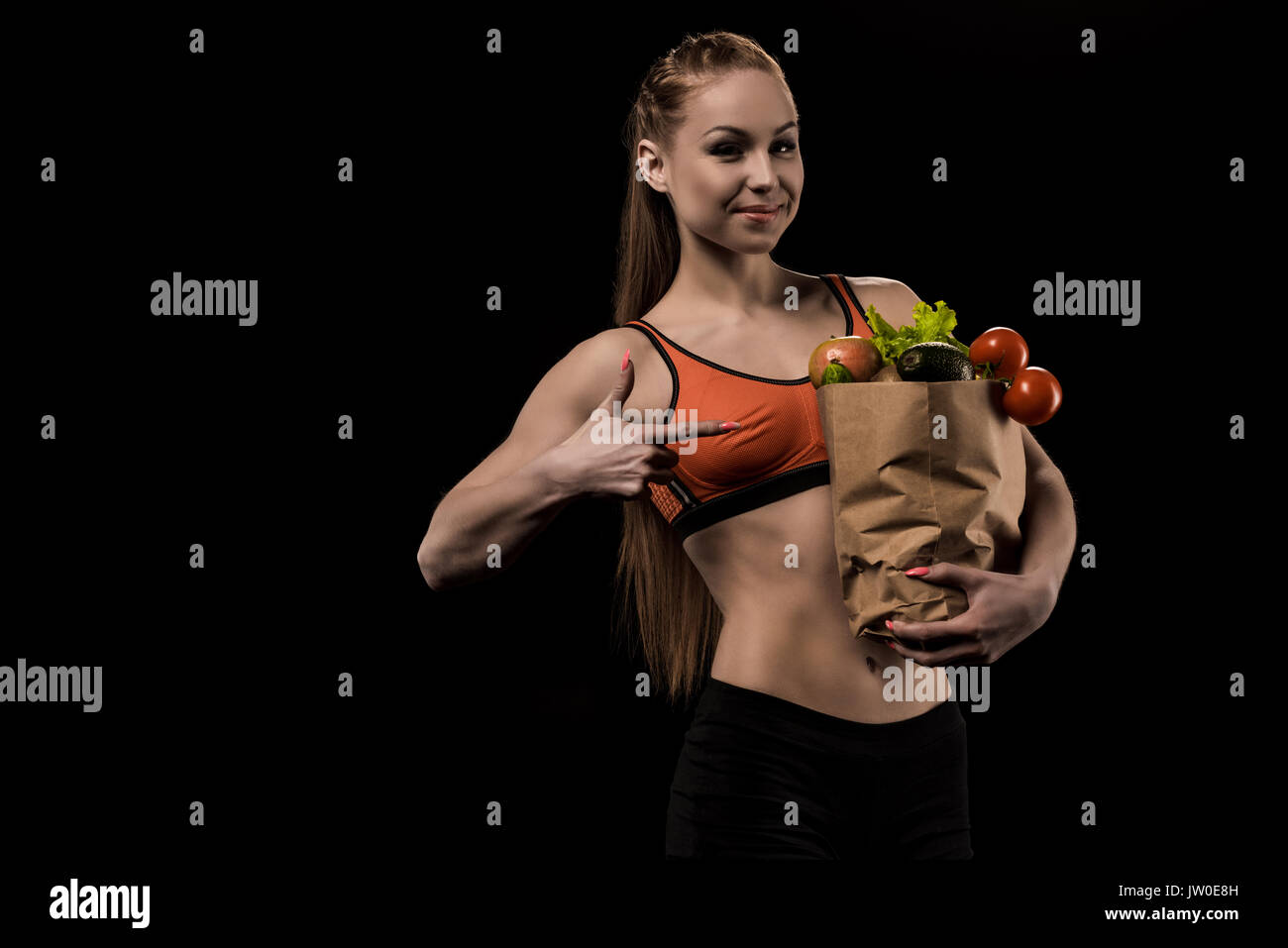 portrait of smiling woman pointing at bag with fresh vegetables isolated on black Stock Photo