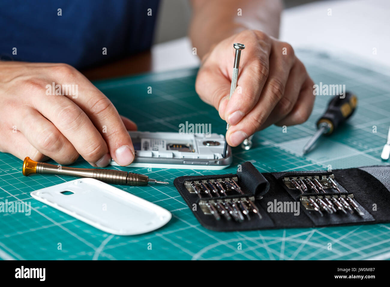 Electronics repair service. Technician disassembling smartphone for inspecting. Stock Photo