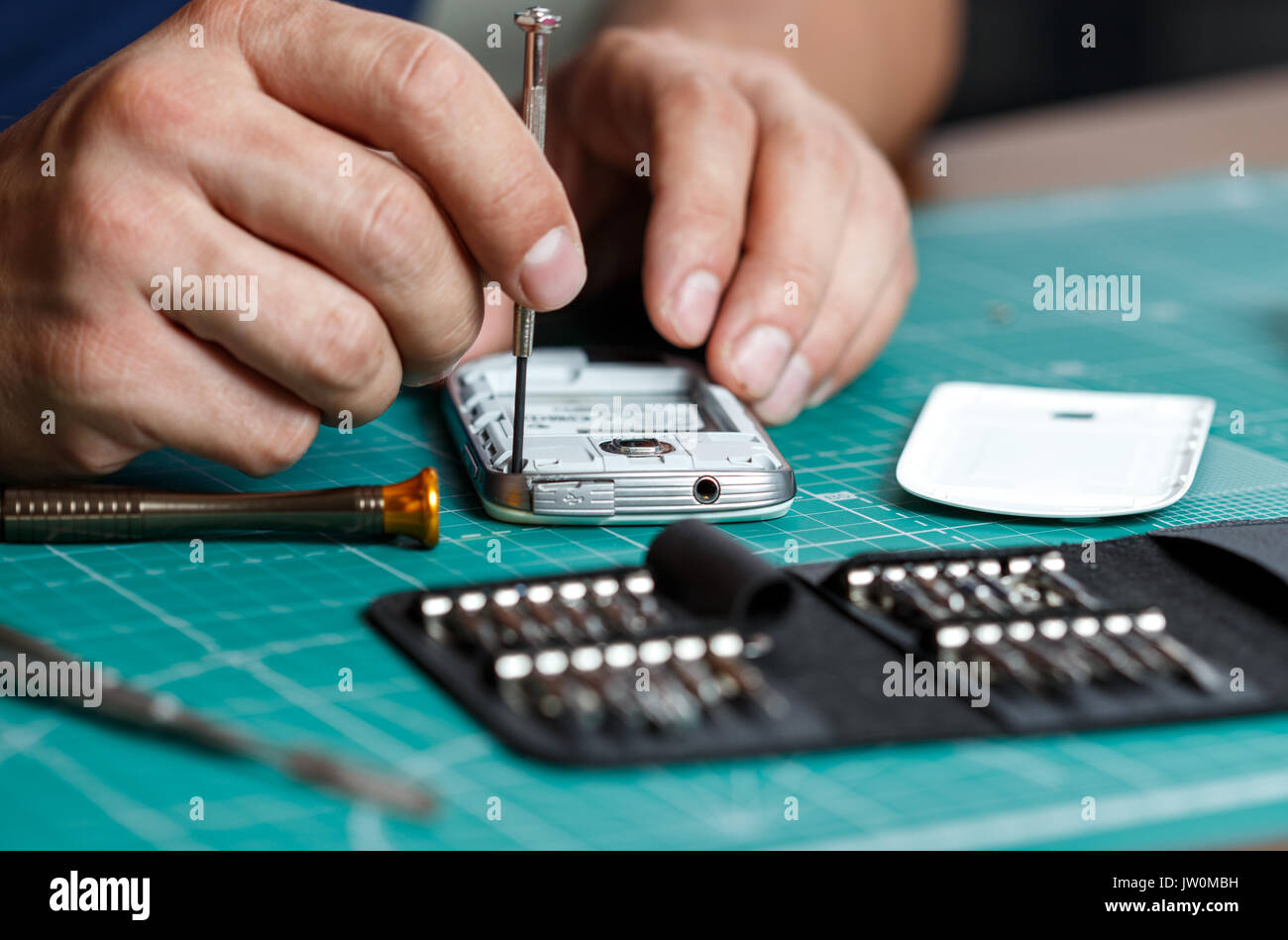 Electronics repair service. Technician disassembling smartphone for inspecting. Stock Photo