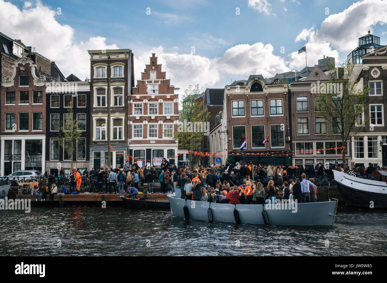 Amsterdam, Netherlands - 27 April, 2017: Local people and tourists dressed in orange clothes ride on boats and participate in celebrating King's Day a Stock Photo