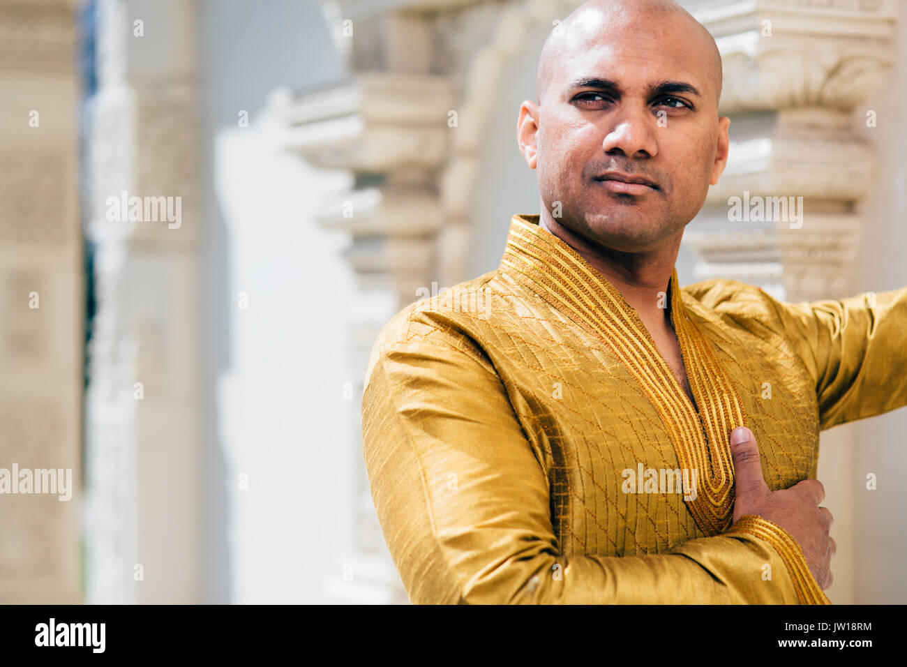 The handsome Indian man wears a gold kurta and posed at a temple. Stock Photo