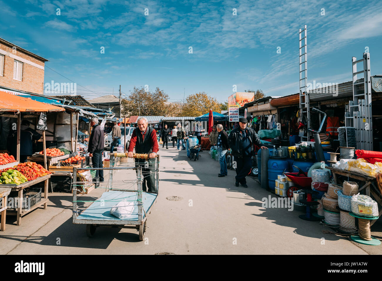 Gori, Shida Kartli Region, Georgia.  Old Man Is Rolling A Cart For The Carriage Of Goods In Local Market In Sunny Autumn Day With Blue Sky. Stock Photo