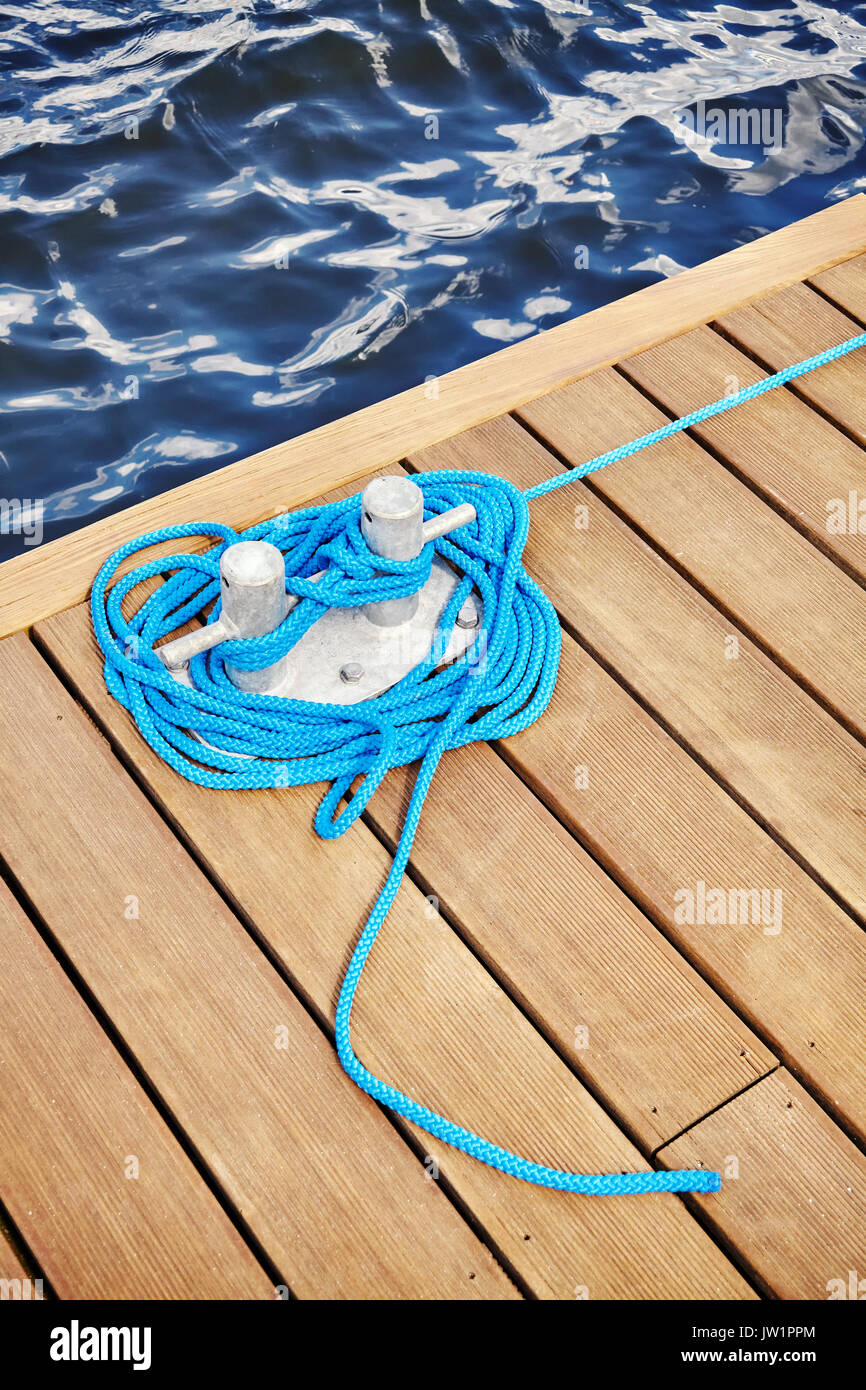 Cleat with blue rope on a wooden pier, travel or safety concept. Stock Photo